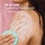 A person using the teal scrubber to apply foaming body wash and scrub to their shoulder. Text reads ‘all‑in‑one hydrating body wash & foaming scrub.